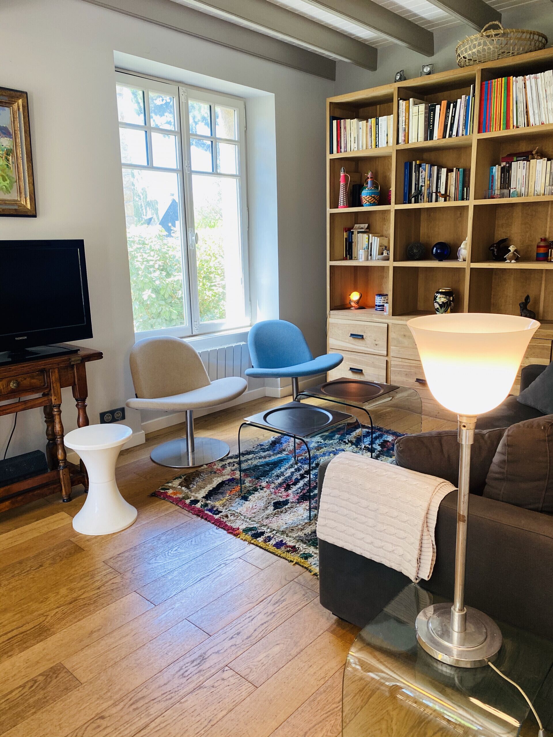 Un salon comprenant un téléviseur, une bibliothèque, un fauteuil bleu, une petite table d’appoint blanche et une lampe.