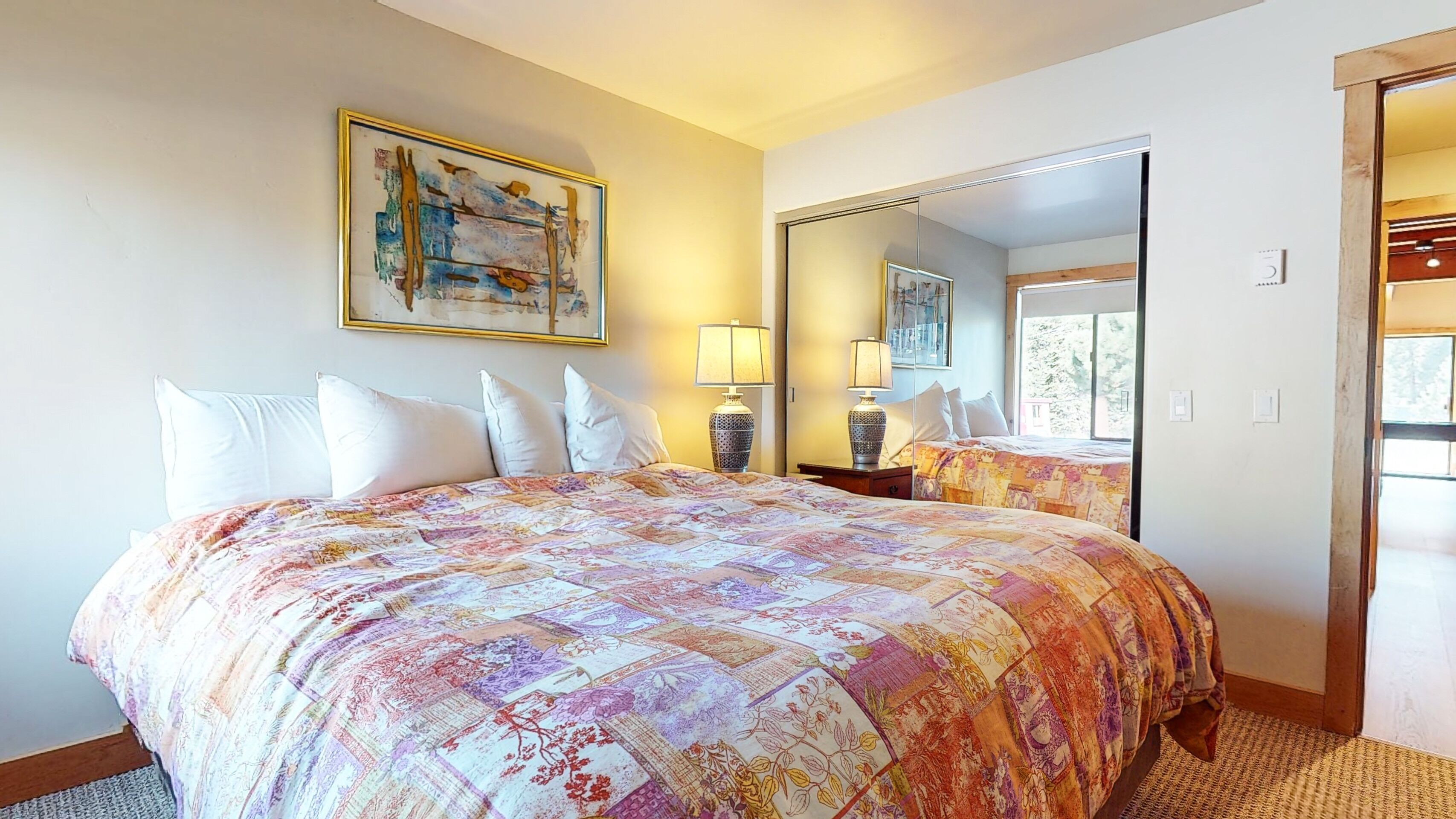 A hotel room with a large bed, a painting on the wall, a mirror, and a window.