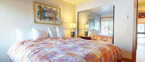 A hotel room with a large bed, a painting on the wall, a mirror, and a window.