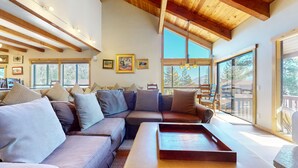 Amplia sala de estar con un sofá modular grande, varios ventanales y techo de madera.