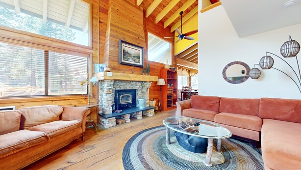 Ein gemütliches Wohnzimmer mit Kamin aus Stein, Holzbalken, einem Glastisch und Ledersofas.