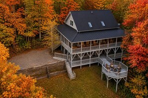 Une maison à deux étages dotée d’un balcon, entourée d’arbres aux feuilles d’automne.