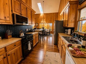 A kitchen with wooden cabinets, a stove, and a dining area with a table and chairs. - The Great Dane: Family and Pet Friendly Mtn Top Cabin, Double Porch, High-Speed (Ferguson)