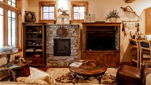 Una sala de estar acogedora con chimenea de piedra, estanterías de madera, televisor y asientos cómodos.