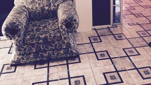 A corner room with a patterned armchair, a tiled floor, and a red wall. - Immaculate 2-bed Apartment in Spanish Town (Spanish Town)