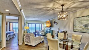 A spacious living area with a balcony, a dining table with chairs, and a large painting on the wall. - Villa Madeira 406 Gorgeous, Beach Front, Top Location! (Madeira Beach)