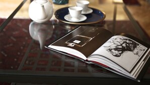 A room with a glass table displaying a teapot, cups, and a magazine. A vase with flowers is in the background. - Luxurious sunlit suite in a prime location with a private city-view balcony, A/C (Budapest)