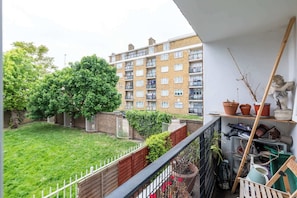 A balcony with a view of a garden, a brick building, and a statue.