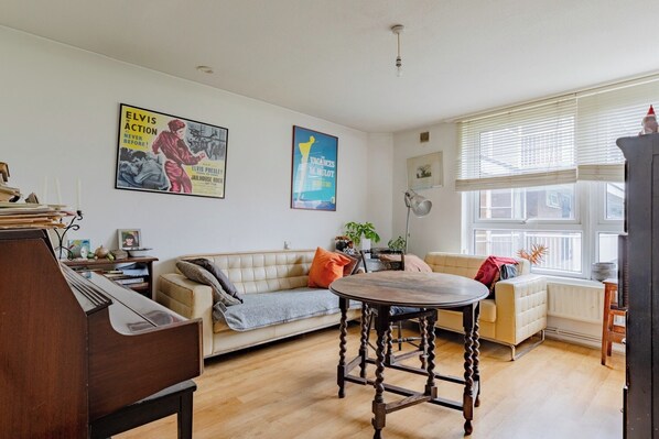 A living room with a piano, a sofa, a table, and two posters on the wall.