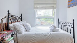 Ein ordentlich bezogenes Bett mit weißen Bettwäsche, einem Metall-Kopfstück und einem Fenster mit Jalousien.