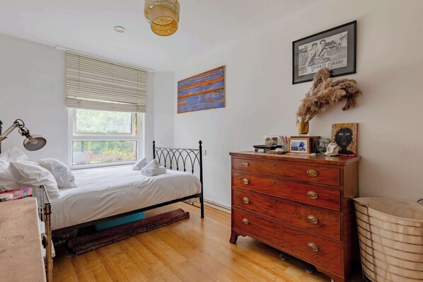 Un dormitorio con cama, cómoda, ventana y obras de arte.