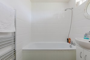 Ein Badezimmer mit einer weißen Badewanne, einem Handtuchhalter, einem Waschbecken mit Toilettenartikeln und einer Duschbrause.