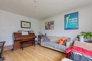 Una sala de estar con un piano, un sofá, un sillón y un cartel en la pared.