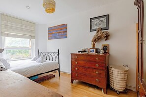 A bedroom with a bed, dresser, artwork, and a window.