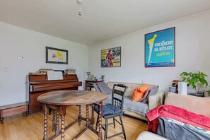 A living room with a piano, a round wooden table, a sofa, and two posters on the wall.