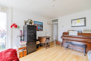 Una habitación con un piano, una estantería, un escritorio y una puerta que da a otra habitación.