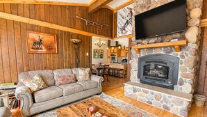 A cozy living room with a stone fireplace, wooden ceiling, and a flat-screen TV mounted above it. - Land's End 3 - The Yeti's Den - Snowshoe, Sunset Views! (Snowshoe)