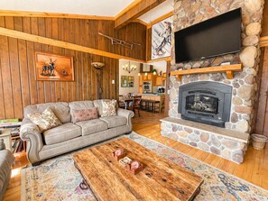 A cozy living room with a stone fireplace, wooden ceiling, and a flat-screen TV mounted above it.
