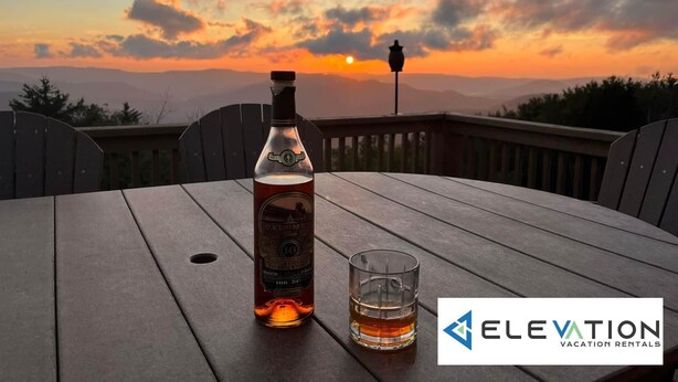 A bottle of Calimete whiskey and a glass on a wooden table with a sunset view. - Land's End 3 - The Yeti's Den - Snowshoe, Sunset Views! (Snowshoe)