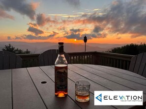 A bottle of Calimete whiskey and a glass on a wooden table with a sunset view. - Land's End 3 - The Yeti's Den - Snowshoe, Sunset Views! (Snowshoe)