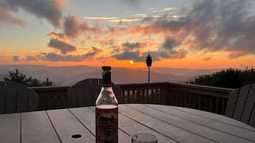 A bottle of Calimete whiskey and a glass on a wooden table with a sunset view.