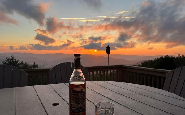 Une bouteille de whisky Calimete et un verre posés sur une table en bois, avec une vue sur le coucher de soleil.