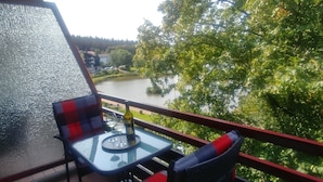 Varanda com mesa e cadeiras, vista para um rio e vegetação.