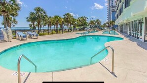 A pool area with lounge chairs and a building with large windows. - SIPPING ON SUNSHINE/OCEANFRONT/PRIME LOCATION (Myrtle Beach)