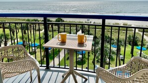 A balcony with a table and two chairs, overlooking a beach and a pool area. - SIPPING ON SUNSHINE/OCEANFRONT/PRIME LOCATION (Myrtle Beach)