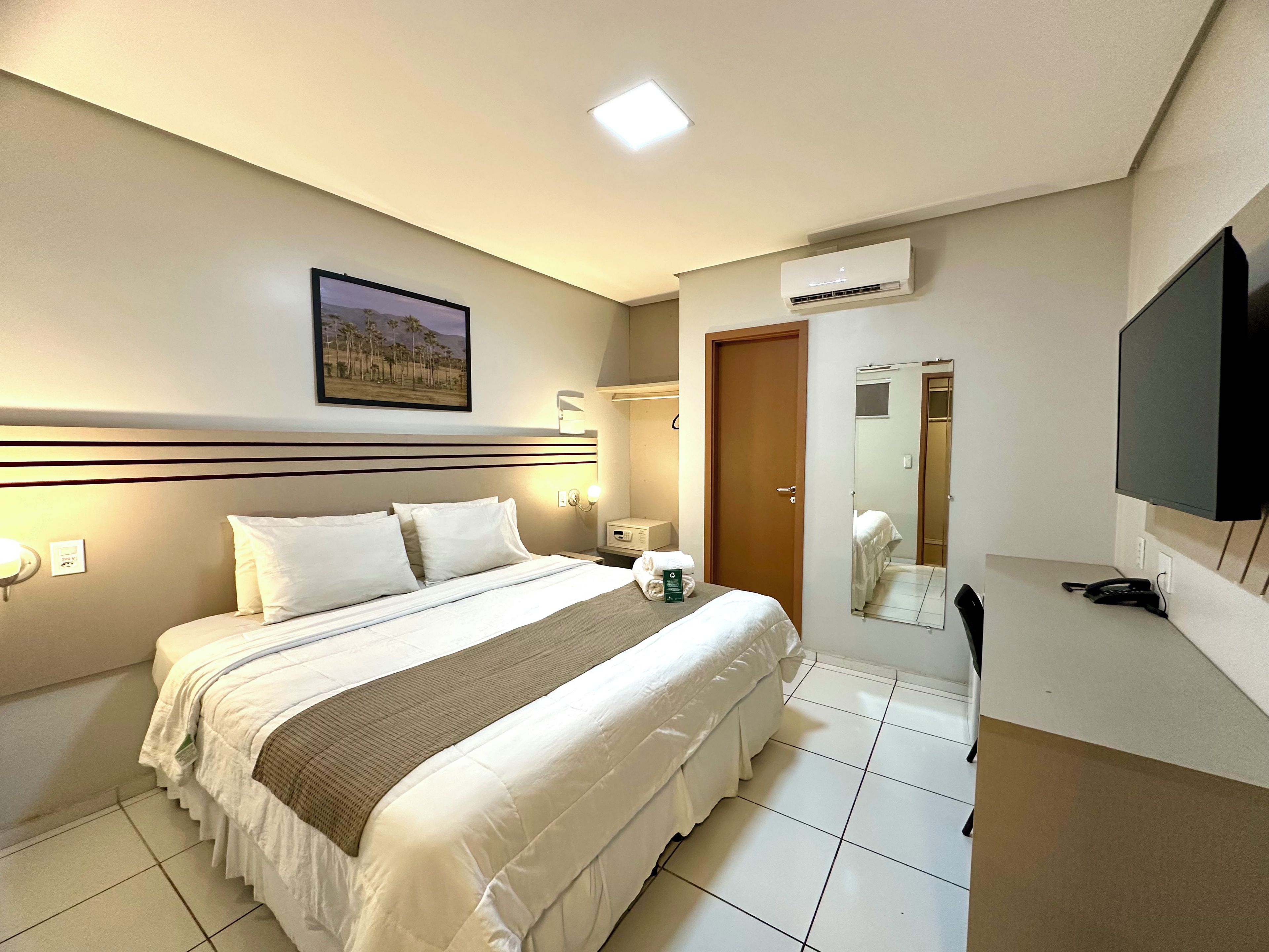 Habitación de hotel con una cama grande, un televisor de pantalla plana, un equipo de aire acondicionado y un espejo de baño.