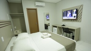 A hotel room with a bed, a desk, a chair, a TV, and a wardrobe.