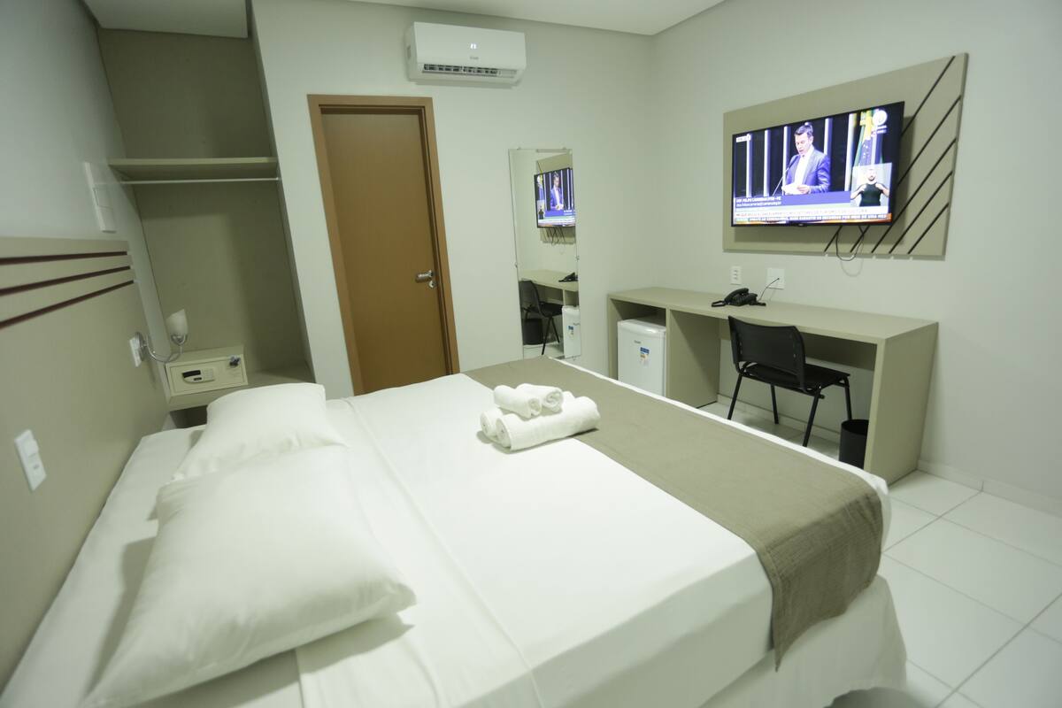 Ein Hotelzimmer mit Bett, Schreibtisch, Sessel, Fernseher und Kleiderschrank.
