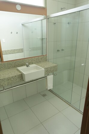 A modern bathroom with a glass shower enclosure, a granite countertop sink, and a large mirror.