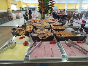 Un bufé con diversos alimentos, entre ellos pasteles, pan y embutidos.