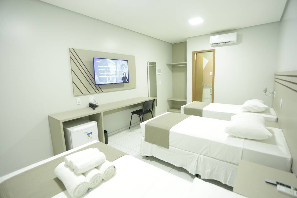 Ein Hotelzimmer mit Schreibtisch, zwei Betten, Fernseher und Kleiderschrank.