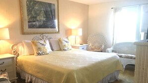 A neatly arranged bedroom with a large bed, two bedside tables, a chair, and a painting on the wall.