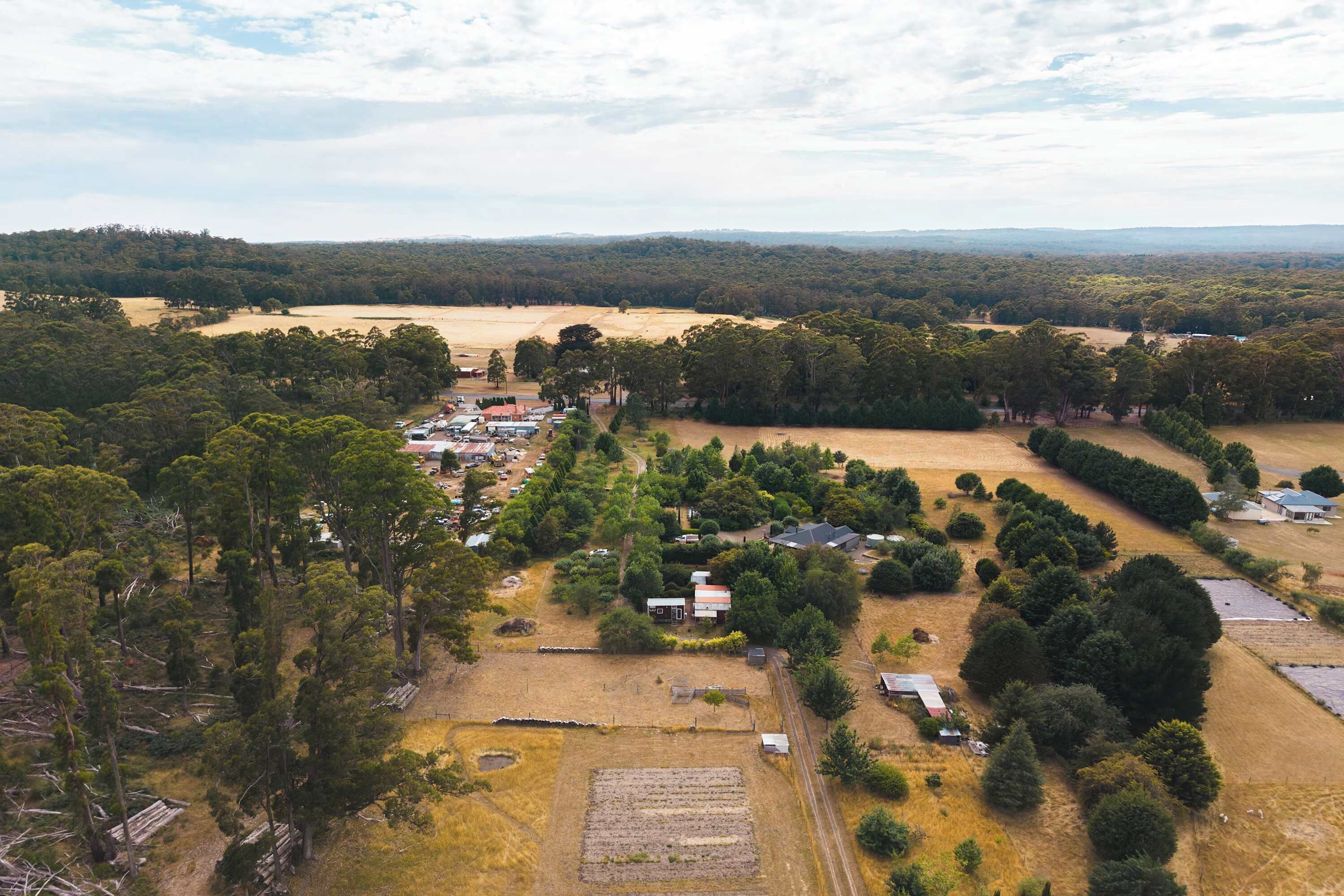 Vista aérea de uma área rural com edifícios dispersos, campos e florestas densas.