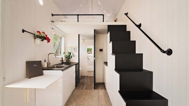 A modern kitchen with white cabinetry, a black staircase, and a small dining area.