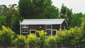 A wooden house with a metal roof, surrounded by dense foliage and a wire fence.