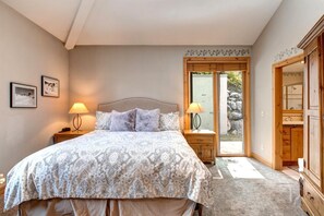 Ein Schlafzimmer mit einem großen Bett, zwei Nachttischen mit Lampen, einem Holzschrank und einer Glasschiebetür, die auf einen Balkon führt.