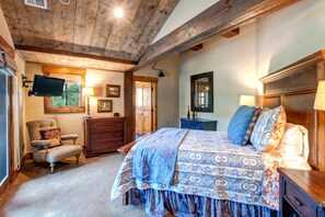 Ein Schlafzimmer mit einem großen Bett, Holzbalkendecke, Fernseher, Kommode und Stuhl.