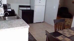 A compact kitchen with a stove, sink, and white refrigerator. There is a dining area with a table and chairs.