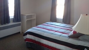 A bedroom with a bed, a bedside lamp, a window with curtains, and a white shelf unit.