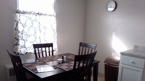 A dining area with a table, chairs, a clock, and a trash bin.