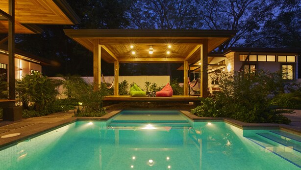 Una piscina con bordo in legno e area relax, immersa nel verde.