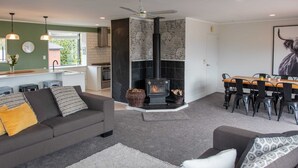 A modern living room with a fireplace, a dining area, and a kitchen. - Pip's Lakeview Retreat (Wanaka)