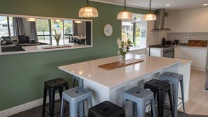 A modern kitchen with a central island, bar stools, pendant lighting, and a large window overlooking a dining area. - Pip's Lakeview Retreat (Wanaka)