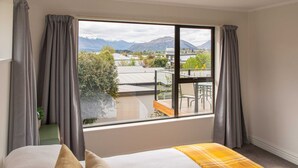 A bedroom with a large window, a bed with a yellow blanket, and a view of a balcony and mountains. - Pip's Lakeview Retreat (Wanaka)