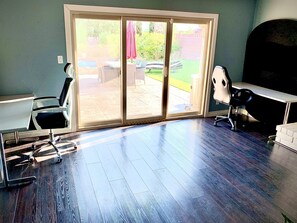 Enjoy a spacious room with a sliding glass door leading to a backyard patio, a desk, office chair, and a small table with chairs.