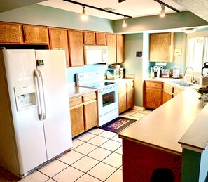 Kitchen features a sink, oven, and refrigerator, with a window above and a door to another room.